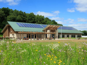 Exterior of Cedar Rapids Indian Creek Nature Center. Wildflowers in foreground, people walking on a sunny day.