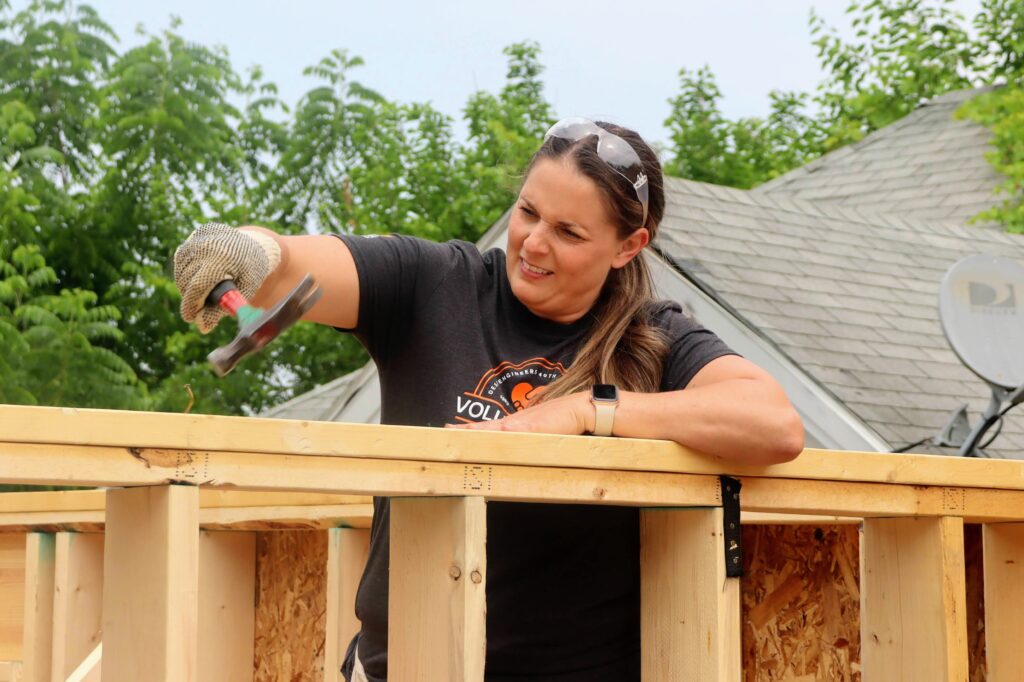 Stephanie on a ladder hammering in a nail on the Habitat for Humanity house. 