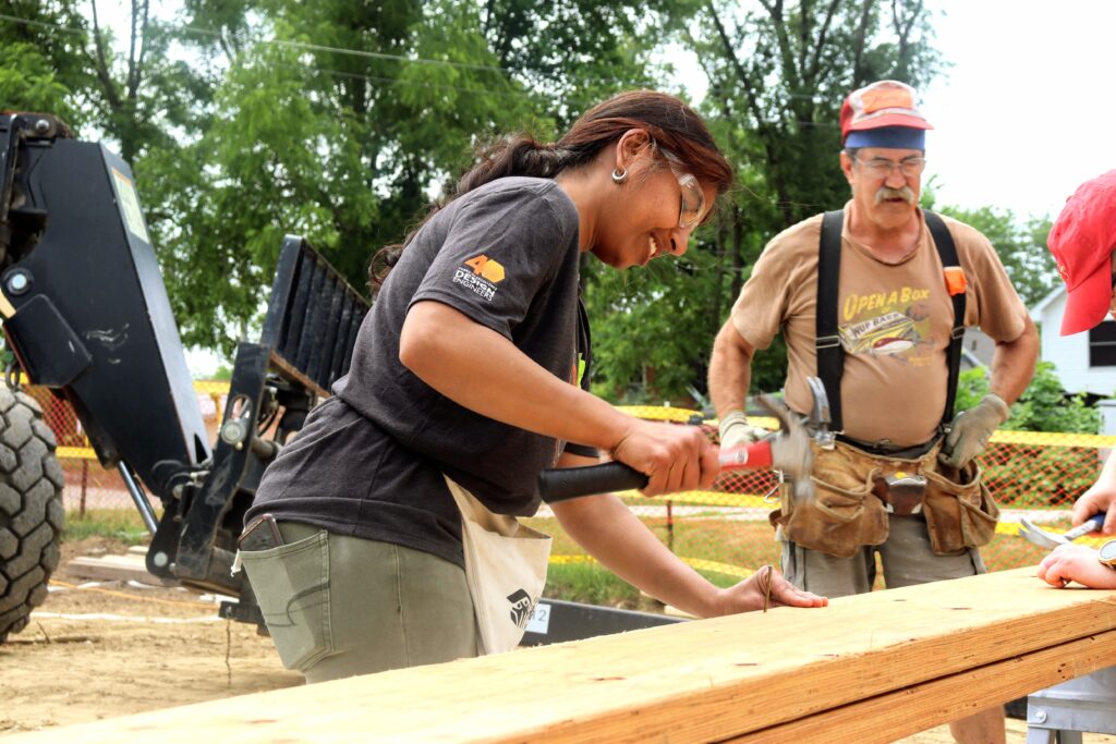 Pallavi hammering in a nail as a Habitat for Humanity volunteer leader stands by.
