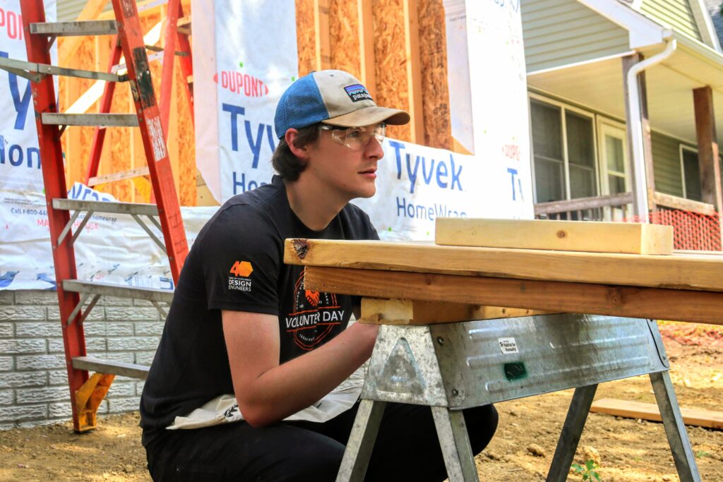 Kyle crouching down to view the alignment of several wood planks at the front of the Habitat for Humanity house.