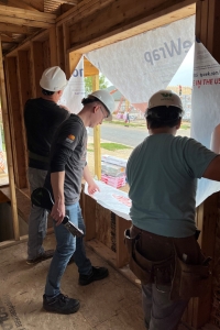 Brad and Jared stapling down loose building paper on a window with a Habitat for Humanity of Dane County volunteer. 